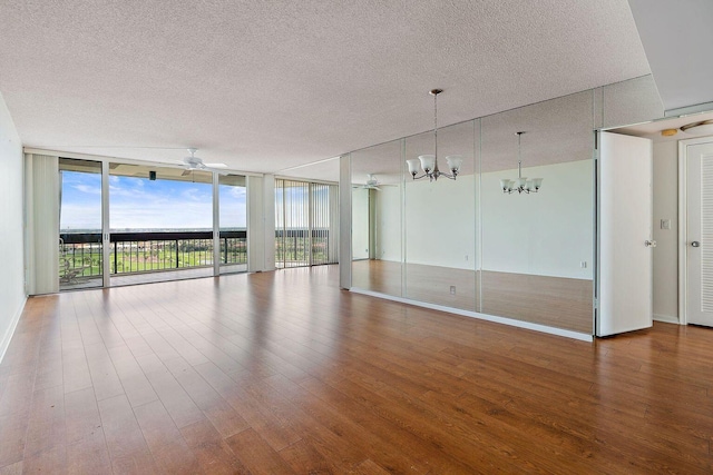 unfurnished room featuring a textured ceiling, ceiling fan with notable chandelier, wood finished floors, baseboards, and expansive windows