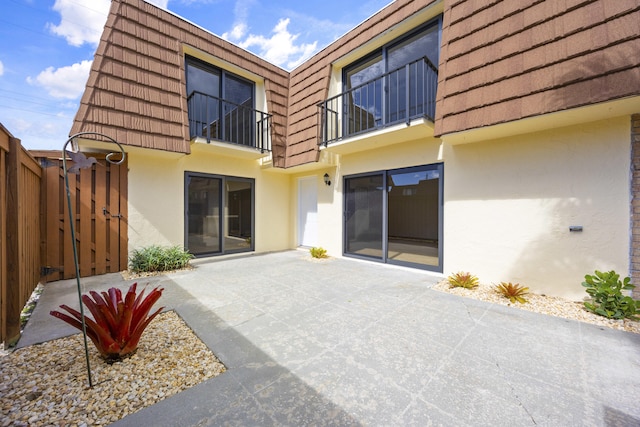 back of house with stucco siding, mansard roof, a gate, a patio area, and fence