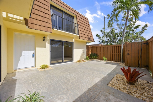 rear view of property with a tile roof, stucco siding, mansard roof, a patio area, and fence