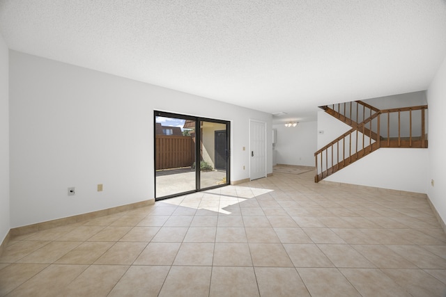 unfurnished living room featuring baseboards, stairway, a textured ceiling, and light tile patterned floors