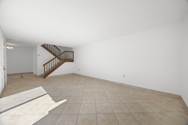 unfurnished living room featuring light tile patterned floors, visible vents, baseboards, and stairs