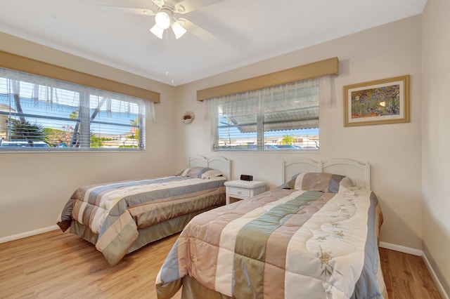 bedroom featuring light wood finished floors, multiple windows, baseboards, and a ceiling fan