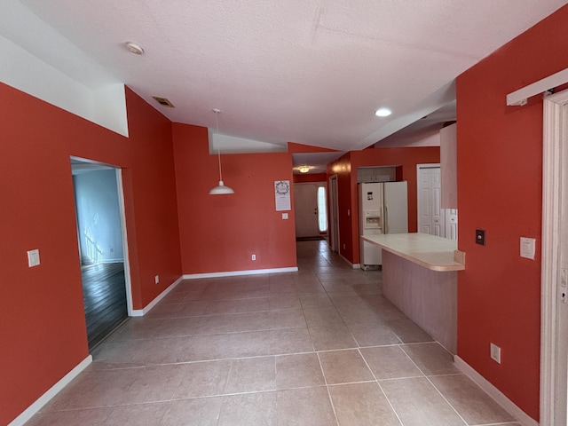 interior space featuring baseboards, vaulted ceiling, a textured ceiling, and light tile patterned flooring