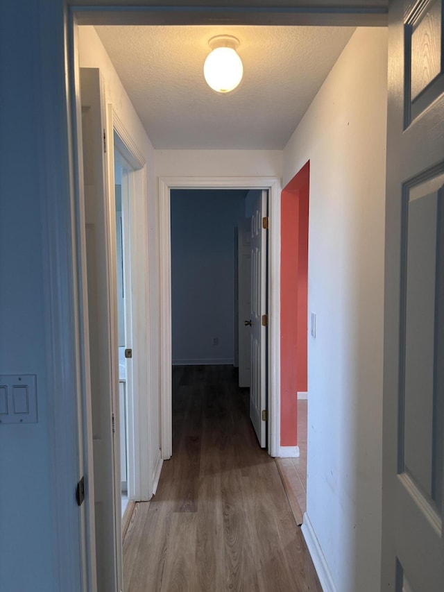 hall with a textured ceiling, wood finished floors, and baseboards