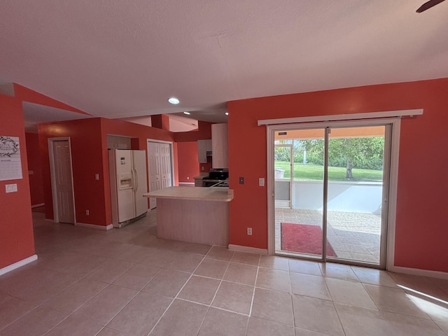 kitchen featuring light tile patterned floors, a peninsula, white refrigerator with ice dispenser, baseboards, and stainless steel range with electric cooktop