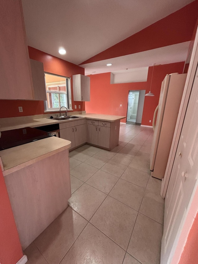 kitchen featuring light tile patterned floors, freestanding refrigerator, vaulted ceiling, a sink, and a peninsula