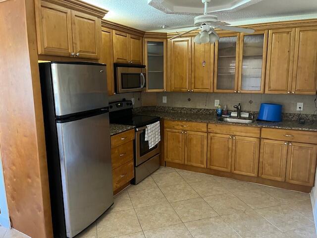 kitchen featuring ceiling fan, glass insert cabinets, brown cabinets, stainless steel appliances, and a sink