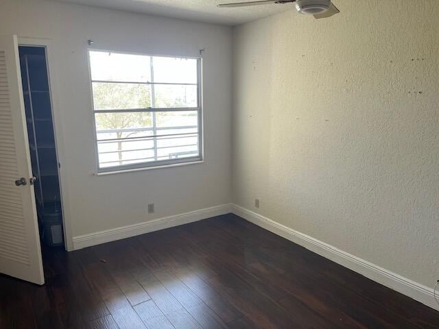 spare room featuring baseboards, dark wood-type flooring, a ceiling fan, and a healthy amount of sunlight