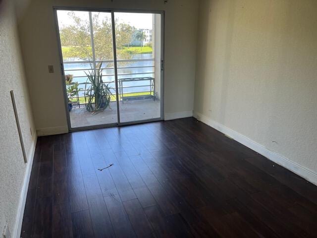 empty room with dark wood-style flooring, a water view, a textured wall, and baseboards