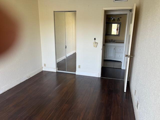 unfurnished bedroom featuring baseboards, visible vents, dark wood finished floors, and a sink