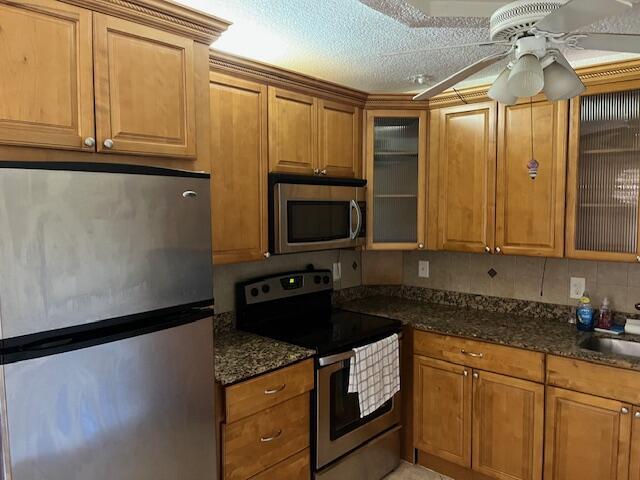 kitchen featuring ceiling fan, appliances with stainless steel finishes, brown cabinetry, and dark stone countertops