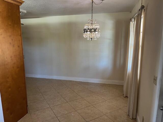 empty room with a notable chandelier, a textured ceiling, baseboards, and light tile patterned floors