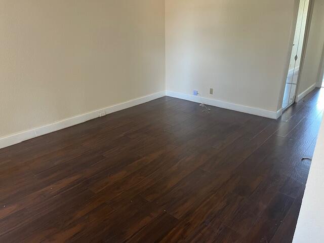 spare room featuring baseboards and dark wood-style flooring