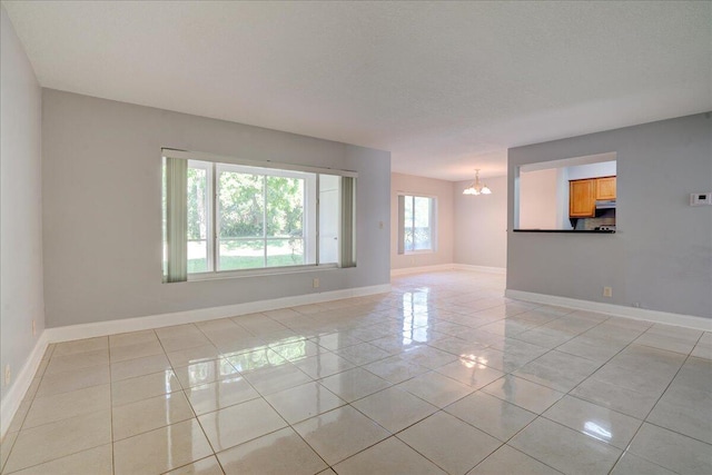 unfurnished room featuring a notable chandelier, baseboards, and light tile patterned floors