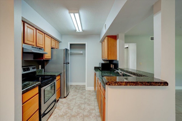 kitchen featuring a textured ceiling, under cabinet range hood, stainless steel appliances, baseboards, and dark stone countertops