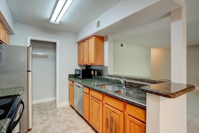 kitchen featuring appliances with stainless steel finishes, dark stone countertops, a sink, and visible vents