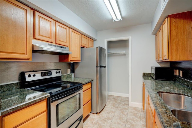 kitchen with decorative backsplash, appliances with stainless steel finishes, dark stone countertops, a textured ceiling, and under cabinet range hood