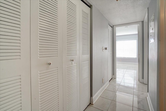 corridor featuring light tile patterned flooring, a textured ceiling, and baseboards