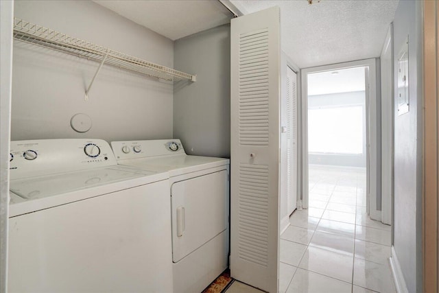 laundry area with a textured ceiling, light tile patterned flooring, washing machine and dryer, laundry area, and baseboards