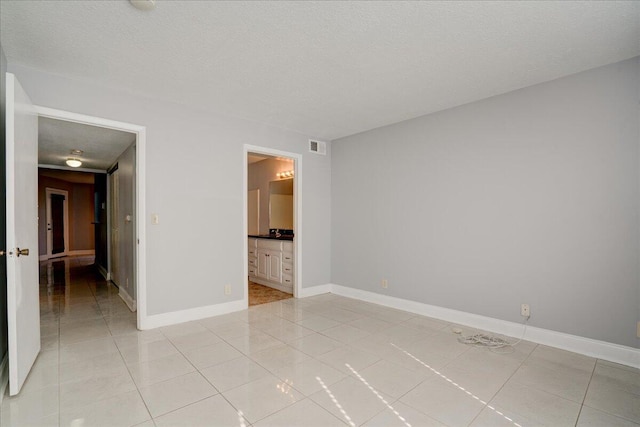 empty room featuring a textured ceiling, light tile patterned floors, visible vents, and baseboards