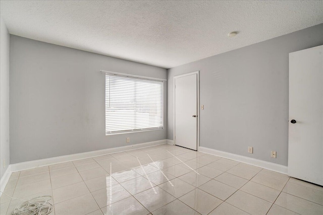 spare room with light tile patterned floors, baseboards, and a textured ceiling