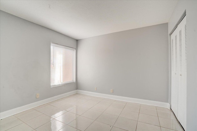 spare room featuring baseboards, a textured ceiling, and light tile patterned flooring