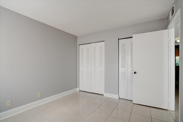 unfurnished bedroom featuring light tile patterned floors, visible vents, baseboards, and two closets