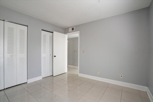 unfurnished bedroom with multiple closets, visible vents, baseboards, and light tile patterned floors