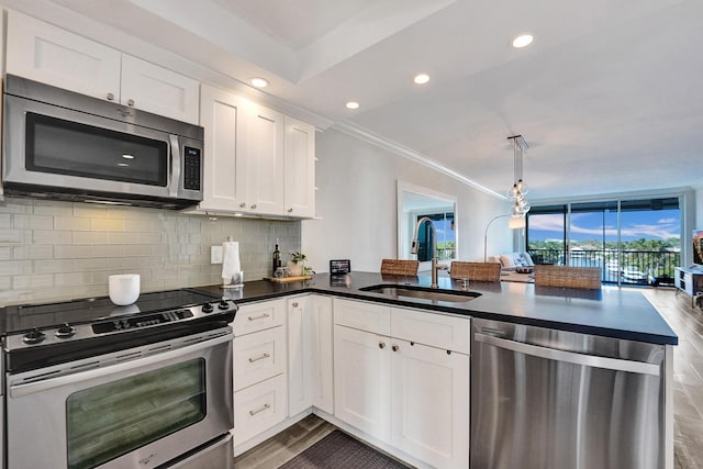 kitchen with stainless steel appliances, a peninsula, a sink, decorative backsplash, and dark countertops