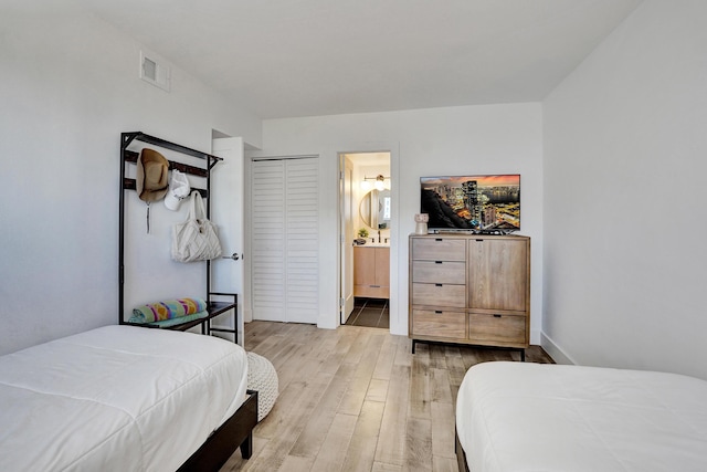 bedroom with baseboards, ensuite bath, visible vents, and wood finished floors