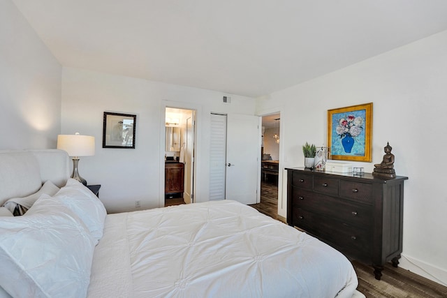 bedroom featuring baseboards, ensuite bath, visible vents, and wood finished floors