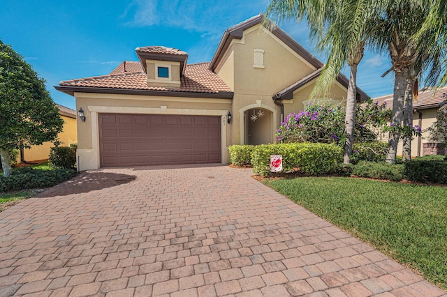 mediterranean / spanish house with a garage, a tile roof, decorative driveway, and stucco siding