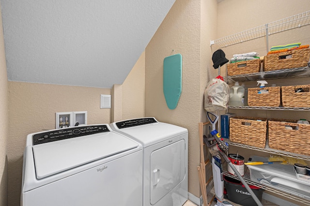washroom featuring laundry area, a textured wall, washer and dryer, and visible vents