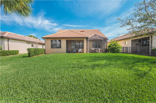 rear view of property with a tiled roof, a lawn, a sunroom, and stucco siding