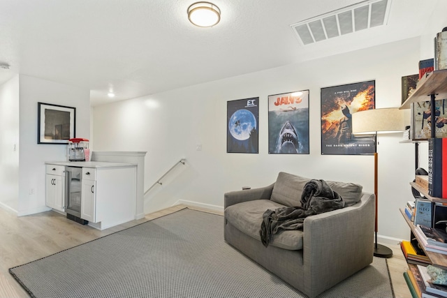 living area featuring beverage cooler, baseboards, visible vents, an upstairs landing, and light wood-type flooring