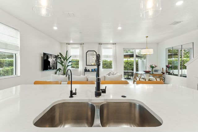 kitchen with visible vents, open floor plan, light countertops, hanging light fixtures, and a sink