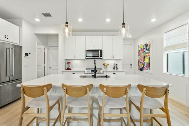 kitchen with visible vents, backsplash, light wood-type flooring, stainless steel appliances, and a sink