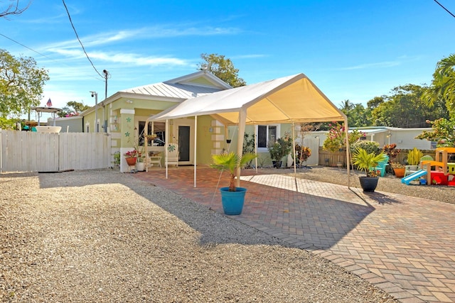 rear view of property featuring metal roof, a patio, a playground, and fence