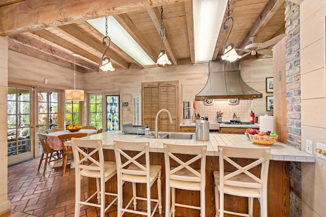 kitchen with brick floor, tile counters, a sink, island range hood, and wooden ceiling