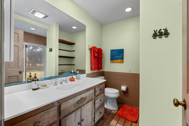 bathroom with tile walls, visible vents, toilet, wainscoting, and vanity