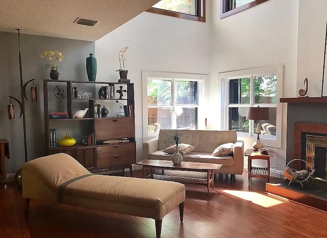 sitting room featuring a fireplace, visible vents, a textured ceiling, wood finished floors, and high vaulted ceiling