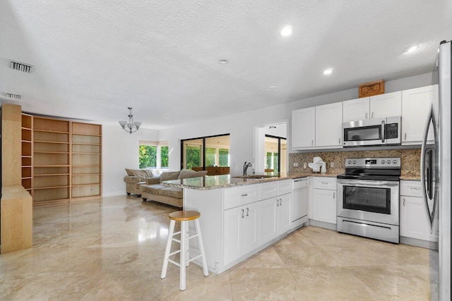 kitchen featuring visible vents, appliances with stainless steel finishes, open floor plan, a peninsula, and a sink