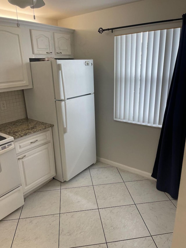 kitchen with light tile patterned floors, tasteful backsplash, freestanding refrigerator, white cabinetry, and range