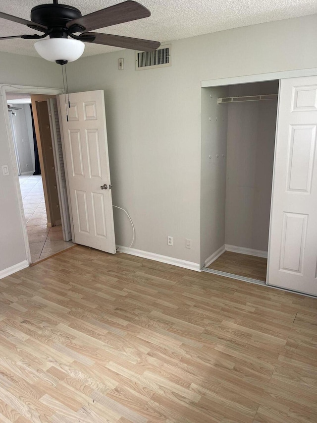 unfurnished bedroom with a closet, visible vents, a textured ceiling, light wood-type flooring, and baseboards