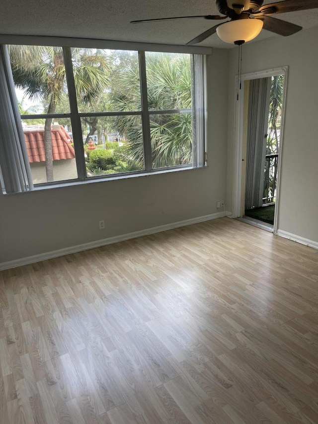 unfurnished room featuring a ceiling fan, plenty of natural light, baseboards, and wood finished floors