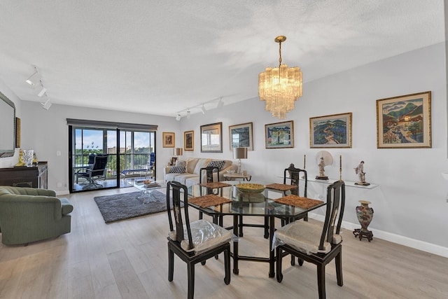 dining room with an inviting chandelier, a textured ceiling, track lighting, light wood-type flooring, and baseboards