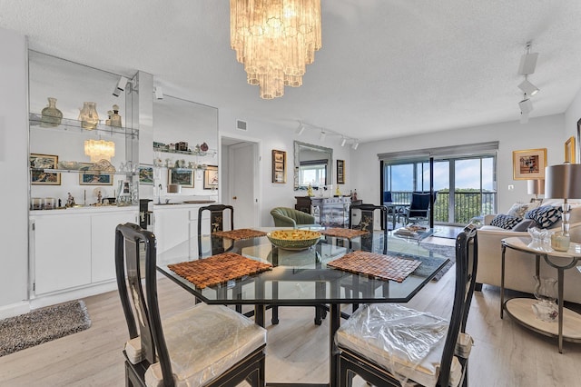 dining space featuring visible vents, rail lighting, light wood-style flooring, a textured ceiling, and a chandelier