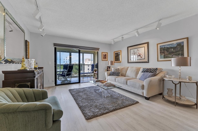 living room with a textured ceiling, light wood-type flooring, baseboards, and track lighting