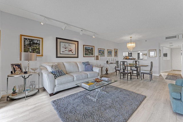 living room with light wood-type flooring, visible vents, a notable chandelier, and a textured ceiling