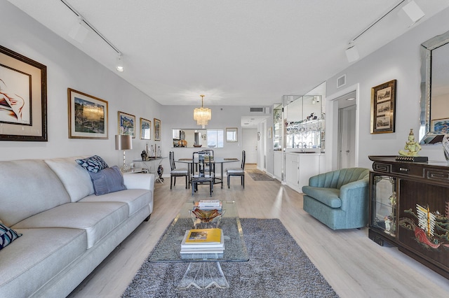 living area featuring a textured ceiling, a notable chandelier, visible vents, light wood-type flooring, and track lighting